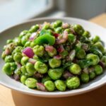 Close-up of a white bowl filled with bright green peas, red onion, and green pepper chunks in a light dressing, representing Cold Southern Pea Salad.