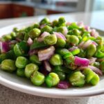 Close-up of a bright, glossy Cold Southern Pea Salad featuring green peas, diced red onion, and green peppers on a white plate.