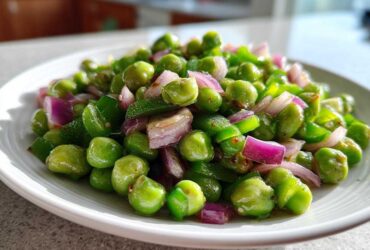 Close-up of a bright, glossy Cold Southern Pea Salad featuring green peas, diced red onion, and green peppers on a white plate.