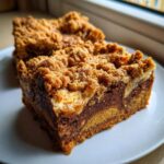 A rich, layered slice of Cookie Butter Biscoff Blondies topped with a thick, golden crumble topping, served on a white plate.