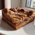 A thick, square slice of rich Cookie Butter Biscoff Blondies with a gooey center and crumbly topping, served on a white plate.