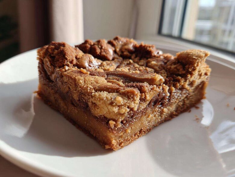 A thick, square slice of rich Cookie Butter Biscoff Blondies with a gooey center and crumbly topping, served on a white plate.
