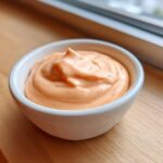 Close-up of creamy, orange-hued copycat Raising Cane's Sauce swirled in a small white dipping bowl.