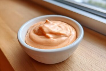 Close-up of creamy, orange-hued copycat Raising Cane's Sauce swirled in a small white dipping bowl.