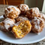 A pile of Cozy Apple Fritter Bites Mini Donut Holes drizzled with white glaze, one is broken open showing the interior.