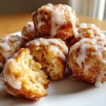 Close-up of several Cozy Apple Fritter Bites Mini Donut Holes drizzled with white glaze, one is broken open showing the soft interior.