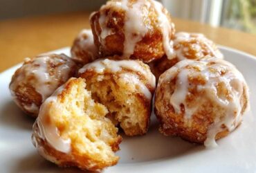 Close-up of several Cozy Apple Fritter Bites Mini Donut Holes drizzled with white glaze, one is broken open showing the soft interior.