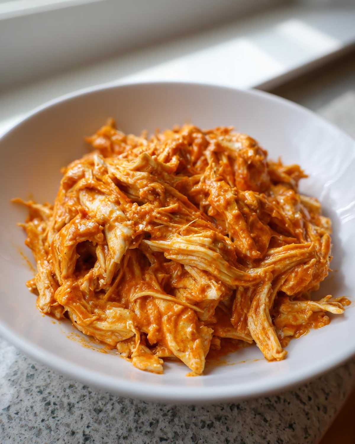 Close-up of shredded chicken coated in a rich, orange sauce, representing Creamy Crockpot Cajun Butter Chicken.