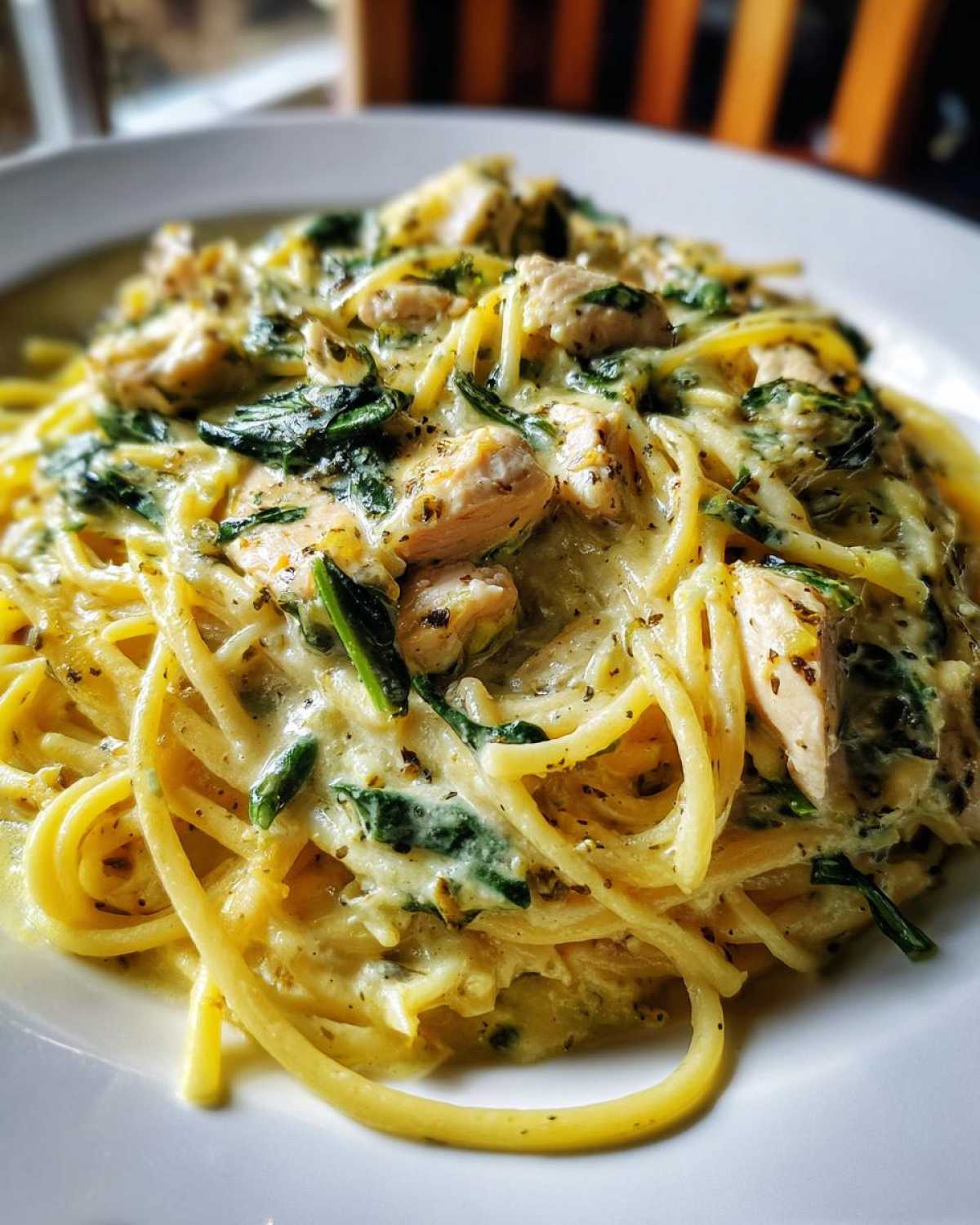 A close-up of creamy Lemon Chicken Pasta tossed with spinach and herbs on a white plate.