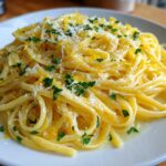 A close-up shot of a serving of creamy lemon pasta, topped with fresh parsley and lemon zest.