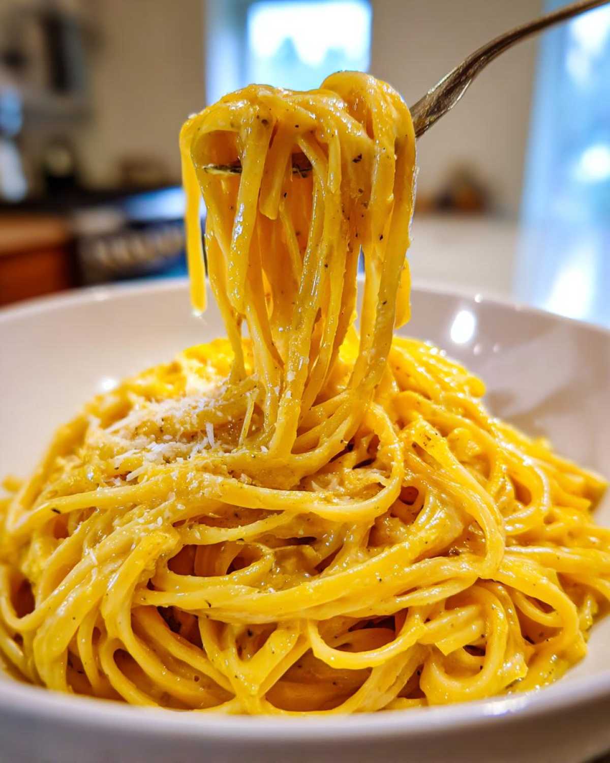 A fork lifts strands of bright yellow Creamy Lemon Pasta coated in a rich sauce, topped with grated cheese.