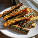 A pile of golden, crispy Air Fryer Zucchini sticks coated in breading and parmesan cheese on a white plate.