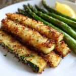 Close-up of Crispy Baked Parmesan Zucchini sticks served with steamed asparagus and a lemon wedge.