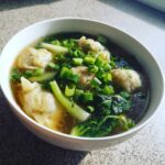 A white bowl filled with hot Dumpling Soup with Frozen Dumplings, garnished heavily with fresh chopped green onions.