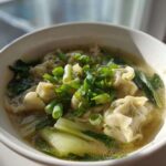 Close-up of a white bowl filled with hot Dumpling Soup with Frozen Dumplings, bok choy, and green onions.