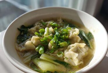 Close-up of a white bowl filled with hot Dumpling Soup with Frozen Dumplings, bok choy, and green onions.