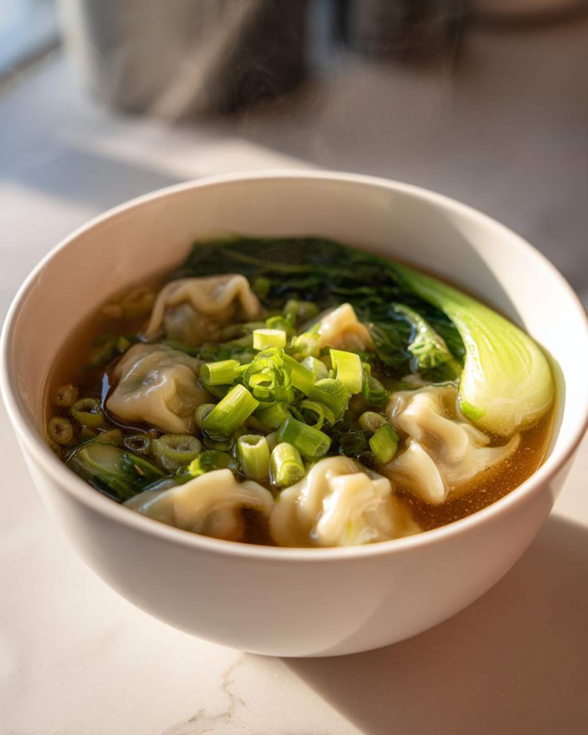 Close-up of a white bowl filled with steaming Dumpling Soup with Frozen Dumplings, topped with bok choy and scallions.
