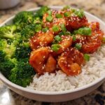 Close-up of a white bowl filled with Honey Garlic Shrimp Bowls, featuring glazed shrimp over white rice and steamed broccoli, garnished with sesame seeds and green onions.