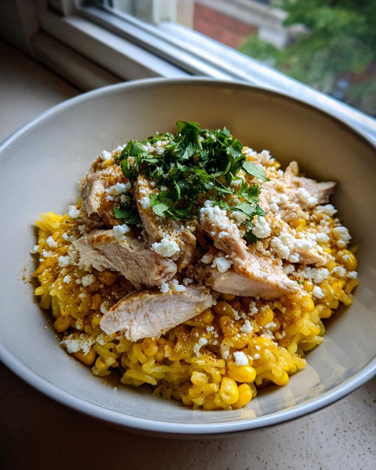 A close-up of the Flavor: Street Corn Chicken Rice Bowl featuring yellow rice, sliced chicken, crumbled cheese, and fresh cilantro.