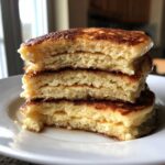 Close-up of a stack of four fluffy Buttermilk Pancakes, showing the airy interior texture and golden-brown edges.