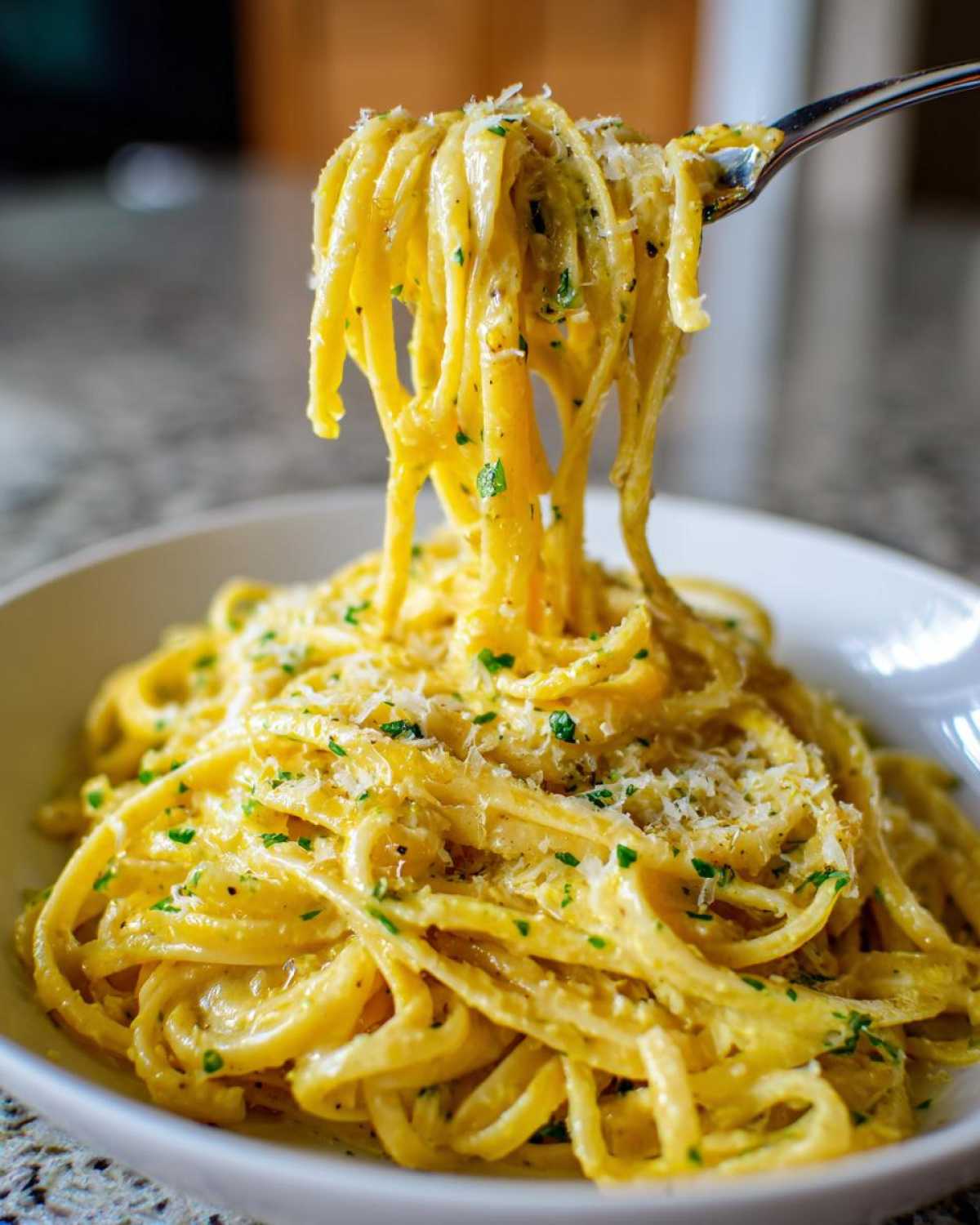 A fork lifting a generous portion of Creamy Lemon Pasta coated in a rich sauce and topped with Parmesan cheese and parsley.