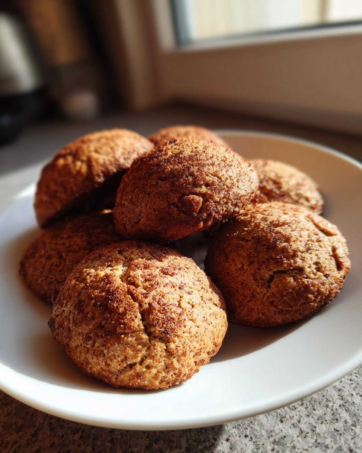 A close-up of several soft, domed Banana Bread Cookies dusted with cinnamon sugar on a white plate.