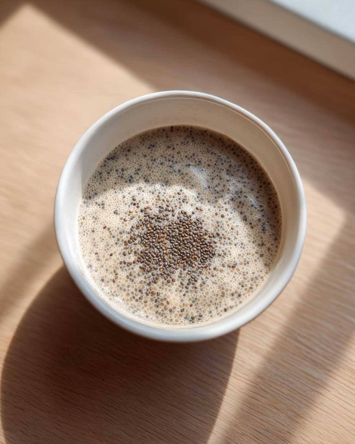 Overhead view of freshly made Chia Seed Pudding in a white bowl, topped with dry chia seeds.