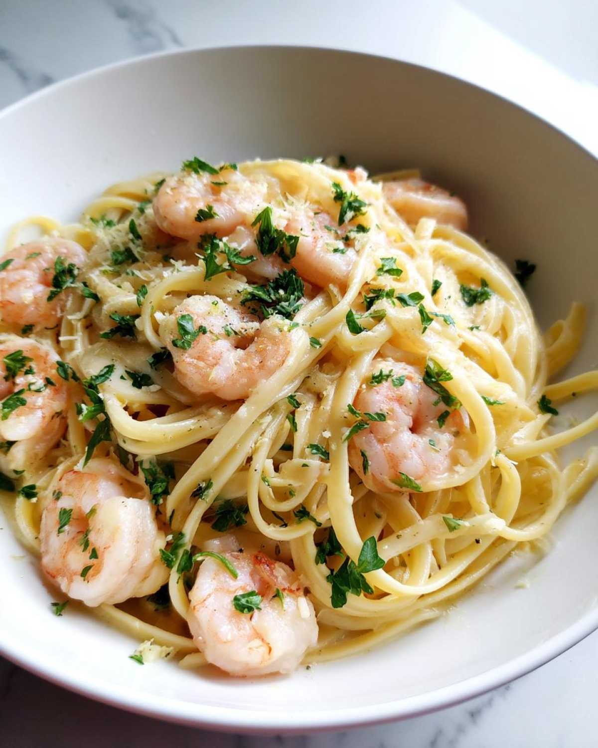 A close-up view of creamy Garlic Butter Shrimp Pasta topped with fresh parsley and grated cheese in a white bowl.