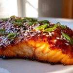 Close-up of a perfectly cooked Gochujang Honey Glazed Salmon fillet topped with sesame seeds and green onions.