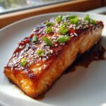 A perfectly cooked fillet of Gochujang Honey Glazed Salmon topped with sesame seeds and green onions.