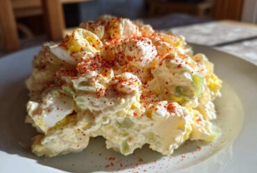 A mound of Grandma's Classic Creamy Potato Salad, featuring potatoes, eggs, celery, and a dusting of red paprika.