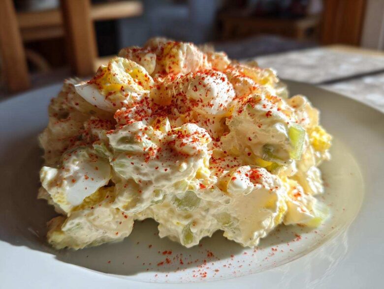 A mound of Grandma's Classic Creamy Potato Salad, featuring potatoes, eggs, celery, and a dusting of red paprika.