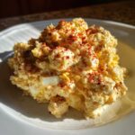 A mound of Grandma's Classic Creamy Potato Salad topped with paprika on a white plate.