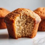 Close-up of a Greek Yogurt Banana Muffins with a bite taken out, showing the soft, moist crumb texture.
