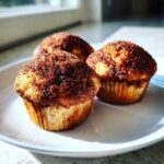 Close-up of three freshly baked Greek Yogurt Cinnamon Muffins topped with a thick cinnamon-sugar crust, sitting on a white plate.