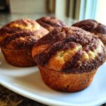 Four freshly baked Greek Yogurt Cinnamon Muffins with a rich cinnamon-sugar swirl topping, presented on a white plate.