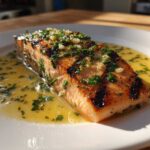 A perfectly cooked piece of Grilled Salmon with Lemon Butter Sauce, topped with fresh herbs and garlic.