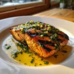 A perfectly cooked fillet of Grilled Salmon with Lemon Butter Sauce, topped with fresh herbs and garlic.
