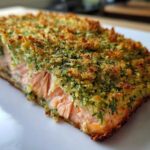 A close-up, cross-section view of a perfectly cooked Herb-Crusted Baked Salmon fillet with a golden, crunchy herb topping.