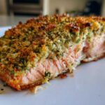Close-up of a moist fillet of Herb-Crusted Baked Salmon showing the flaky pink interior and golden, crunchy herb topping.