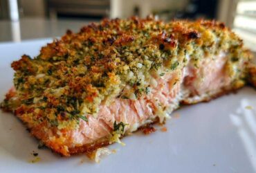 Close-up of a moist fillet of Herb-Crusted Baked Salmon showing the flaky pink interior and golden, crunchy herb topping.