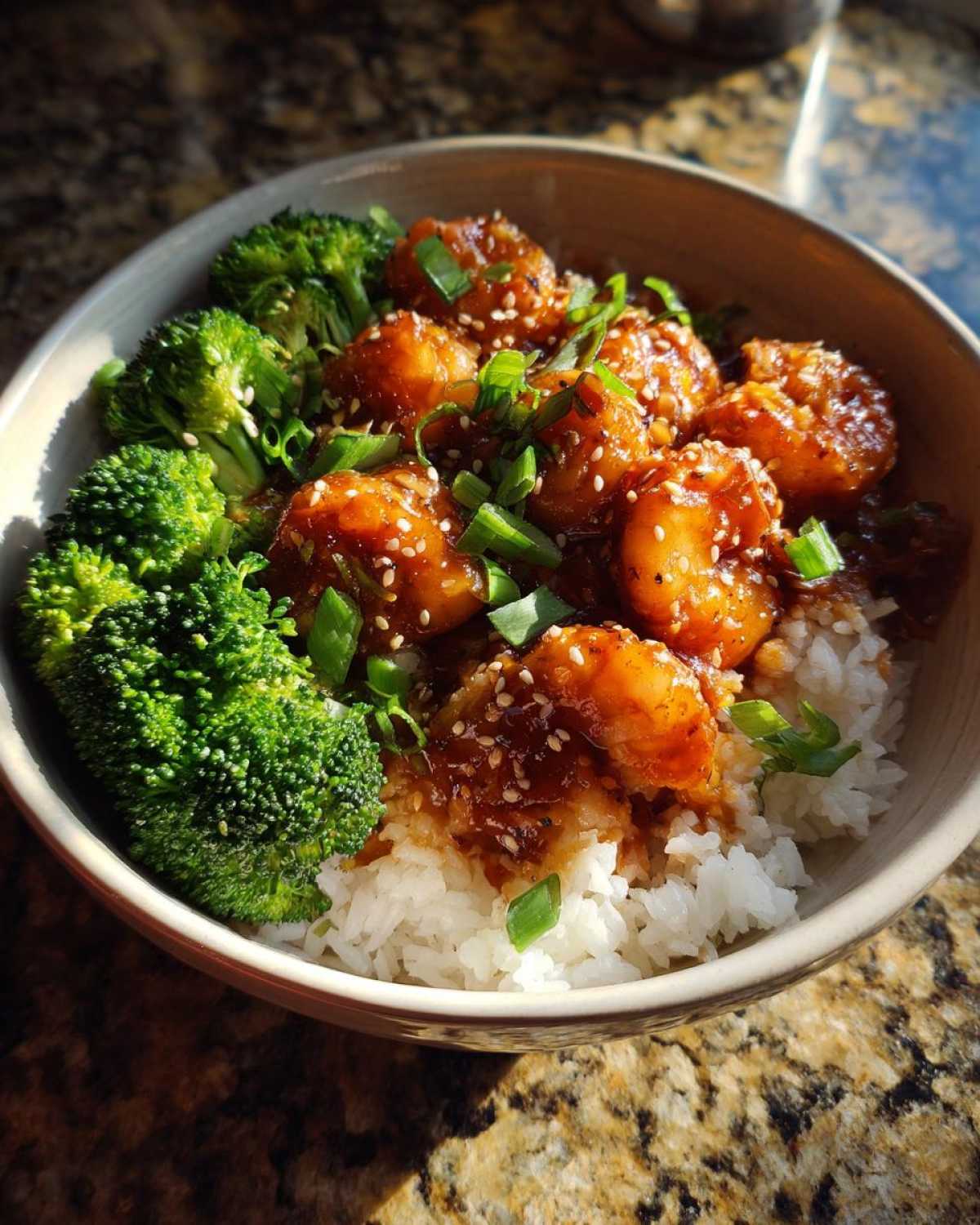 A bowl filled with white rice topped with glossy Honey Garlic Shrimp, steamed broccoli florets, and green onions.