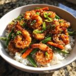 A close-up of a white bowl filled with Honey Garlic Shrimp Bowls, featuring glazed shrimp over rice with green beans and carrots, topped with sesame seeds.