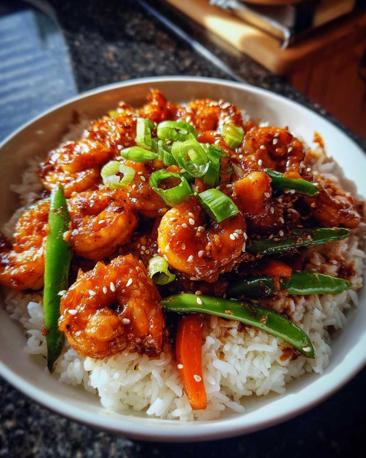 A close-up of a serving of Honey Garlic Shrimp Bowls featuring glazed shrimp over white rice with green onions and snap peas.