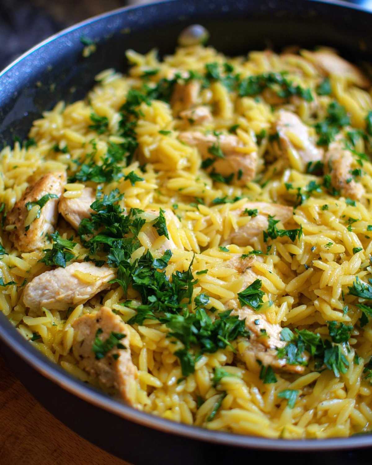 Close-up of Lemon Chicken and Orzo dish cooked in a skillet, topped with fresh parsley.