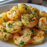 A close-up shot of cooked Lemon Garlic Shrimp piled on a white plate, glistening with butter sauce and fresh parsley.