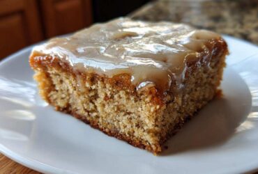 A close-up of one square of Moist Banana Bars with Browned Butter Vanilla Glaze on a white plate.