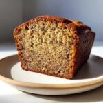 A close-up, cross-section view of a moist slice of Banana Bread showing dark flecks of mashed banana.