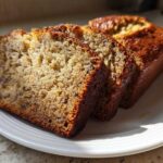Three thick slices of moist Banana Bread displayed on a white plate, showing a rich, golden-brown crust.