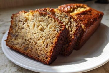Three thick slices of moist Banana Bread displayed on a white plate, showing a rich, golden-brown crust.